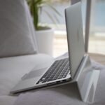 A modern laptop sits open on a cozy couch with natural sunlight streaming in.